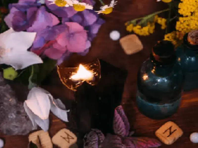 Imagen de pétalos de flores, runas, vela encendida, frascos con hierbas e incienso, representando el apoyo en el camino espiritual y mágico. Contáctanos!