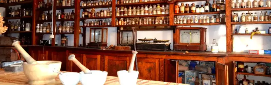 Aviso Legal: Fotografía de un boticario antiguo con estanterías llenas de frascos, un mostrador con morteros y balanzas, representando un entorno clásico.