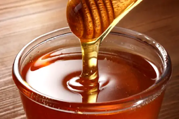 Recipiente con miel y cuchara de madera, ingredientes naturales utilizados en el baño de pies purificador para restaurar energía y atraer bienestar.