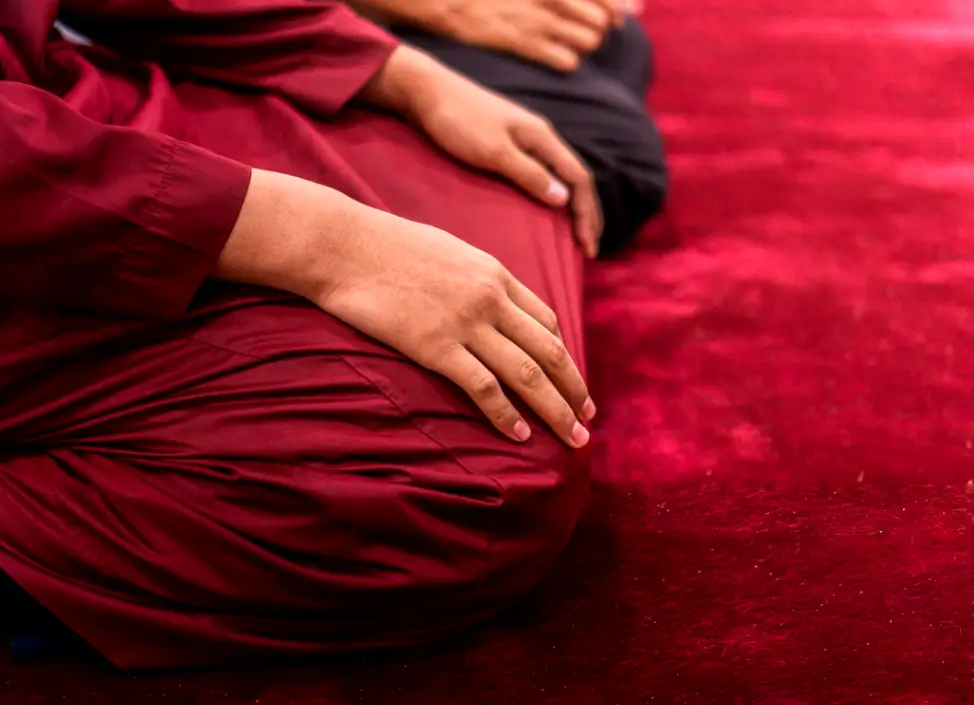 Hombre musulmán rezando sobre una alfombra roja en interior, concentrado en decretos de poder