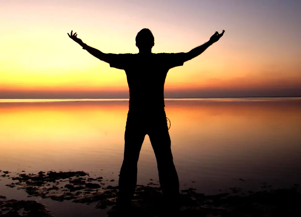 Silueta de hombre de pie junto al mar al atardecer, pronunciando decretos de poder