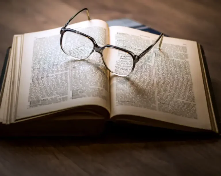 Manual de Ética de la Guardiana: Las Leyes de No Interferencia y el Sagrado Libre Albedrío. 11 Primer plano de un par de lentes descansando sobre las páginas de un libro antiguo abierto, simbolizando la claridad y el discernimiento en la Ética de la Guardiana.