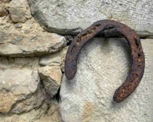Primer plano de una herradura de hierro vieja y oxidada colgando de un muro de piedras rústico, simbolizando las señales de que el universo te responde y la buena fortuna.