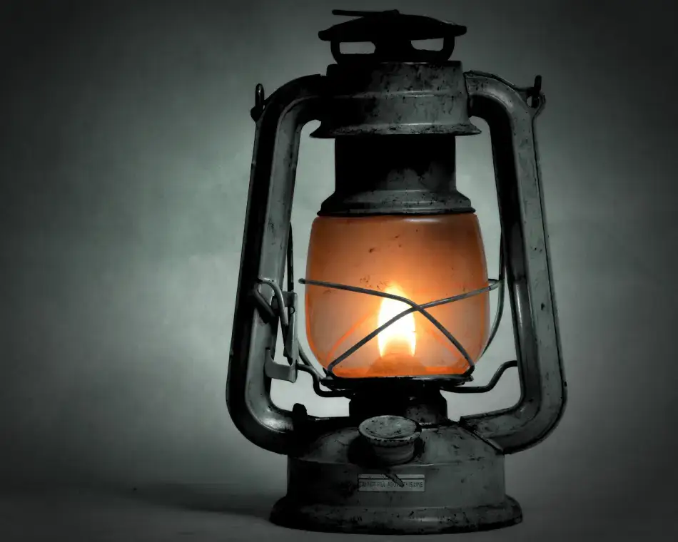 Farol antiguo de metal con la mecha encendida emitiendo luz cálida en la oscuridad, representando la guía en el exorcismo digital.