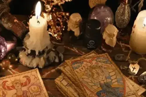 Invocaciones secretas y arte oculto con Velas encendidas rodeadas de cartas de tarot, runas, piedras preciosas, una cruz de madera